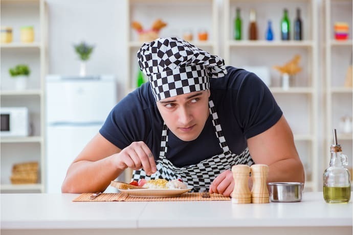 Homem usando avental de cozinha e touca de cozinha que combinam.
