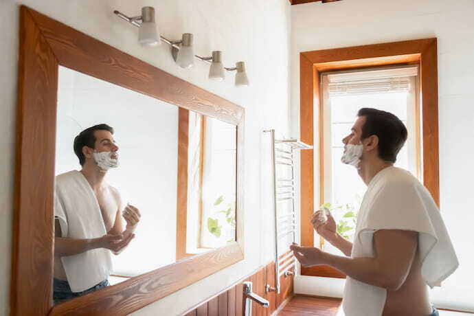 Homem fazendo a barba no espelho.