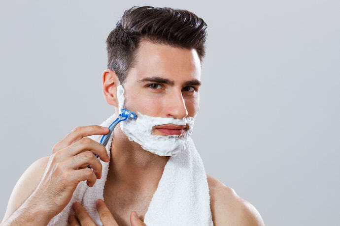 Homem fazendo a barba com espuma de barbear e lâmina azul.