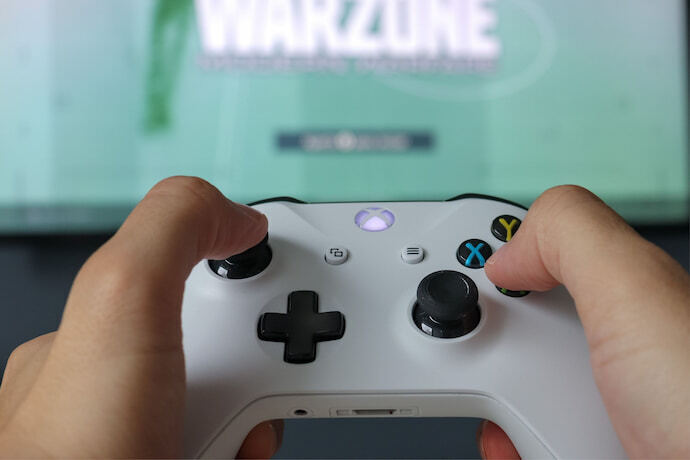 Pessoa jogando Warzone com controle de Xbox One branco.