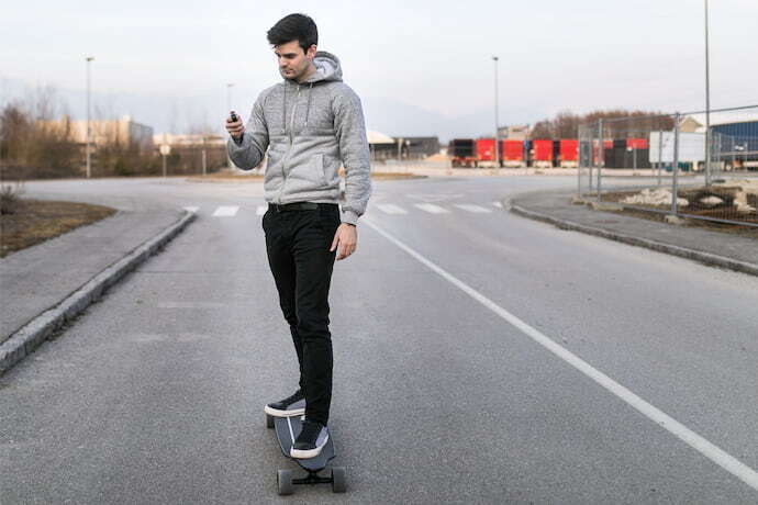 Homem andando em skate elétrico segurando controle remoto.