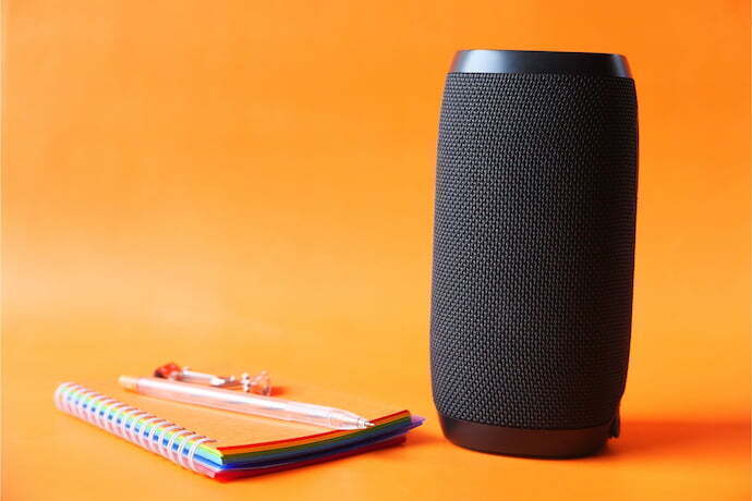 Smart speaker preta ao lado de caderninho laranja.