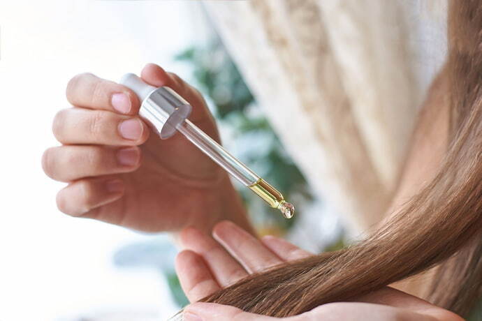 Pessoa aplicando óleo de rícino nos cabelos.