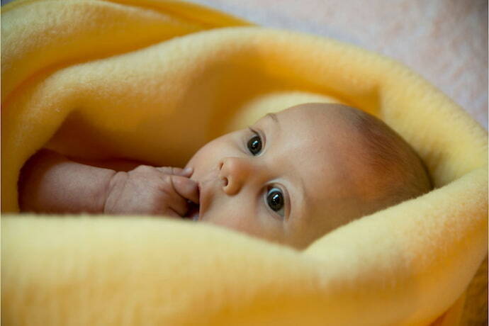 Bebê enrolado em coberto amarelo.
