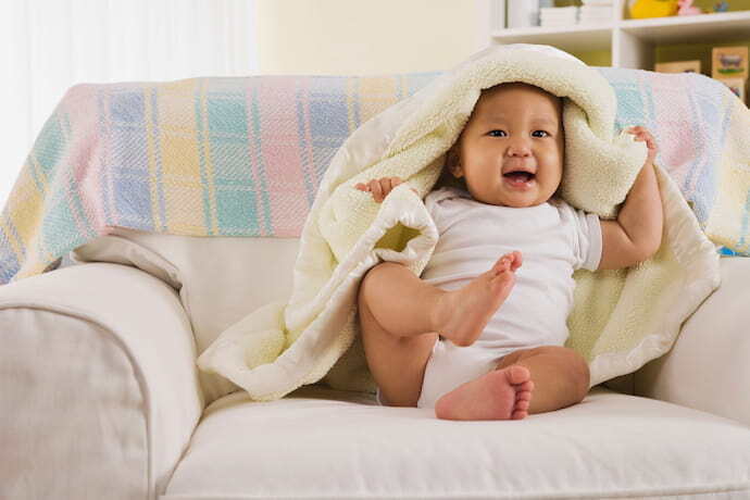 Bebê sentando sorrindo com cobertor amarelo em volta.