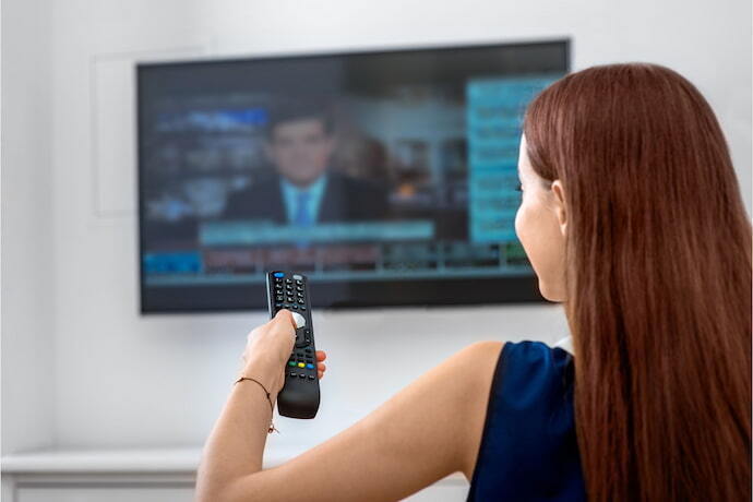 Mulher assistindo TV com Alexa com controle na mão.