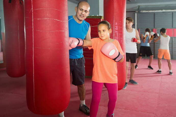 Professor ensinando menina a lutar com luva de boxe.