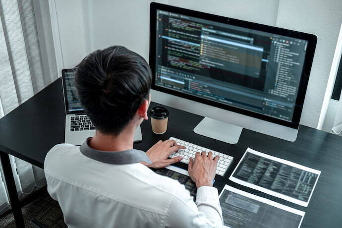Homem programando em desktop e notebook