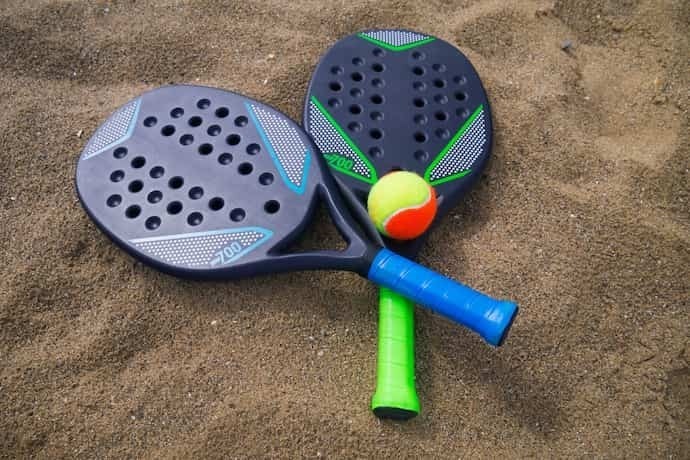 Duas raquete de Beach Tennis coloridas com bolinhas na areia.