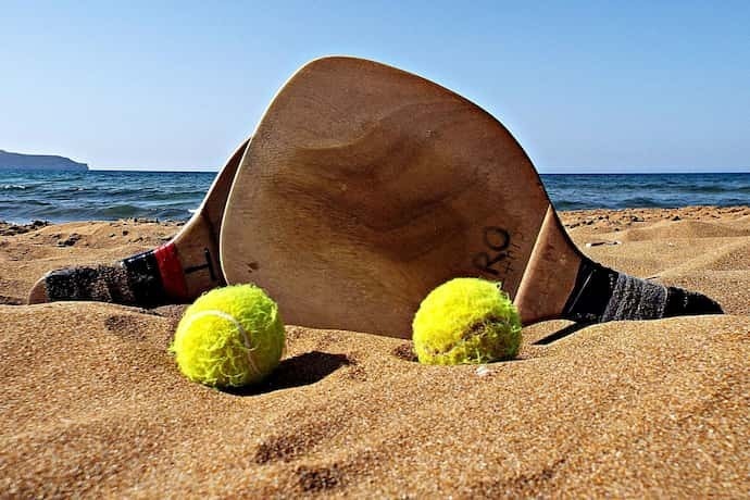 Duas raquetes de Beach Tennis de madeira com bolinhas de tênis em areia.