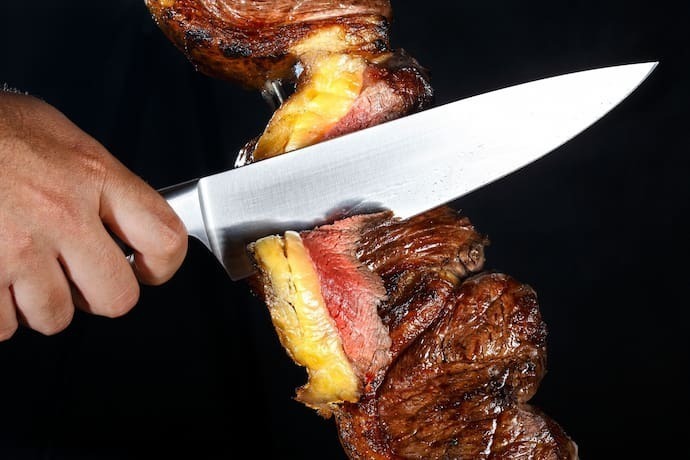 Pessoa cortando carne de churrasco com faca para churrasco