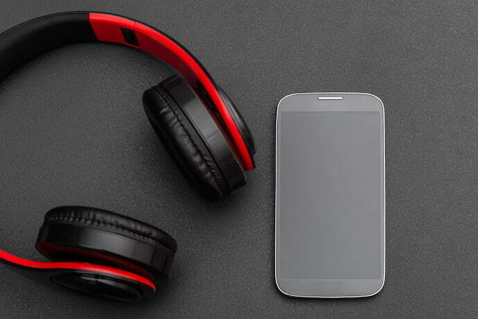 Headphone Bluetooth vermelho e preto com celular ao lado.