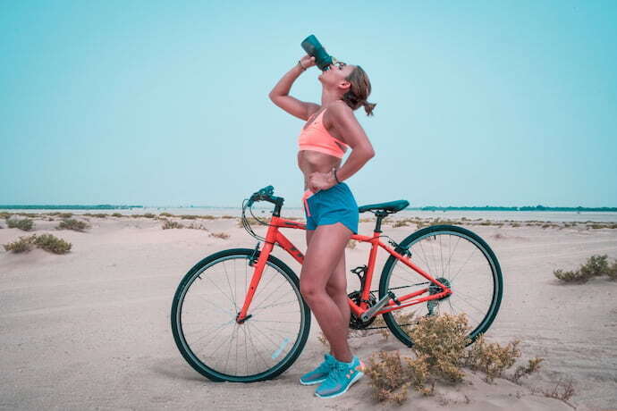 Mulher tomando água em bicicleta.