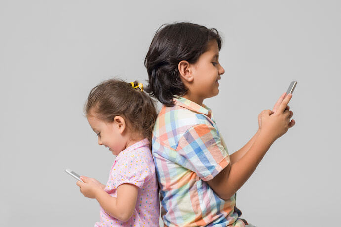 Duas crianças de costas uma para a outra, ambas usando celulares