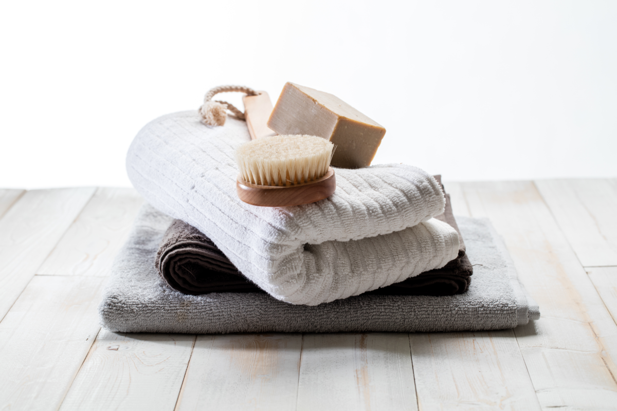 Sobre a mesa toalhas, escova corporal e sabão em barra.