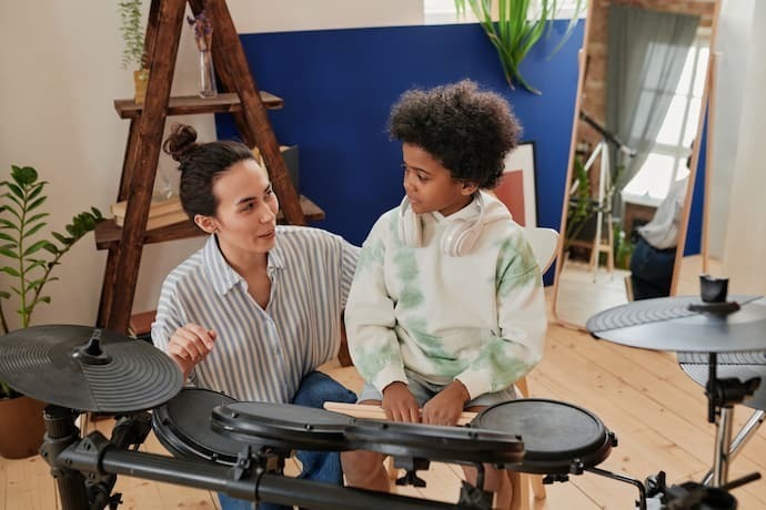 Mulher ensinando menino a tocar bateria eletrônica.