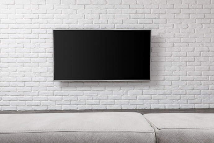 Televisão preta pendurada na parede cinza