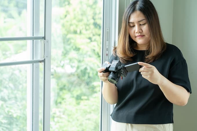 Mulher segurando câmera com as duas mãos em frente ao peito, observando o visor digital