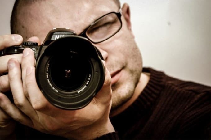 Homem de óculos segurando uma câmera com um dos olhos fechados