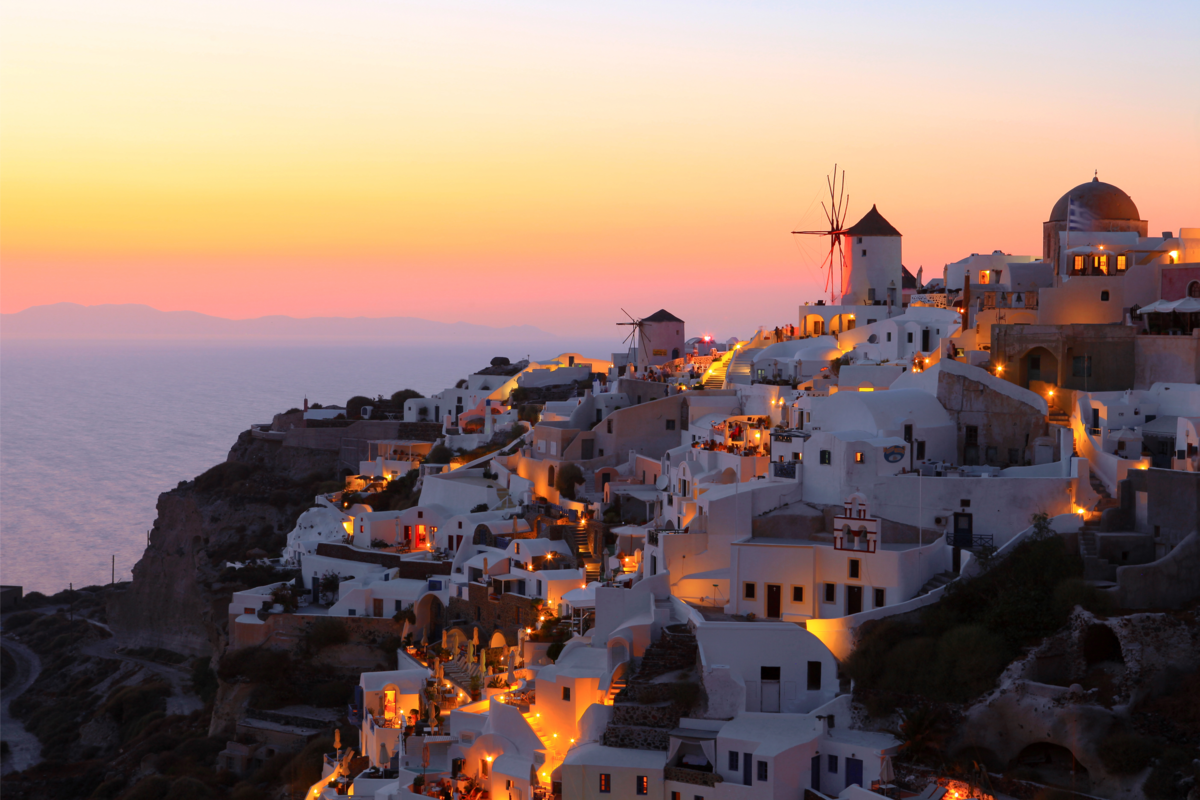 Um pôr do sol, várias casinhas iluminadas por luzes e um mar a frente