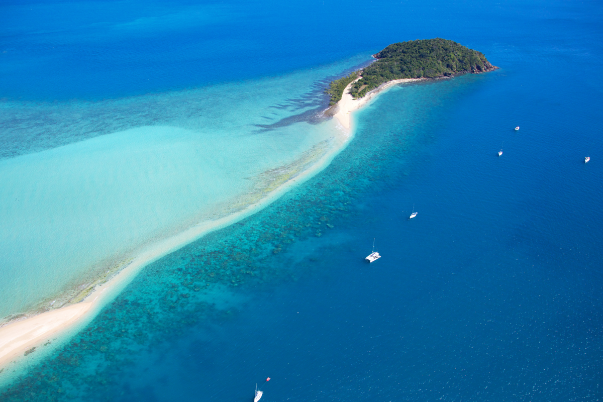 Uma ilha vista de cima, água cristalina e alguns pequenos barcos