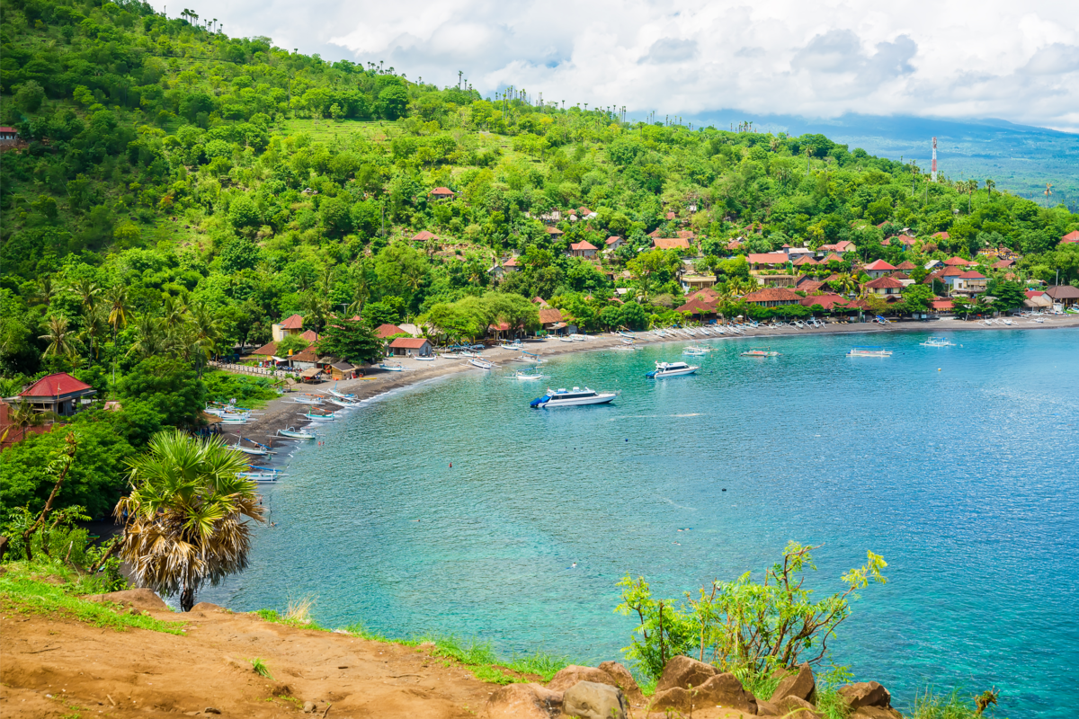 Vista de uma praia cercada pela floresta, casas e barcos no mar