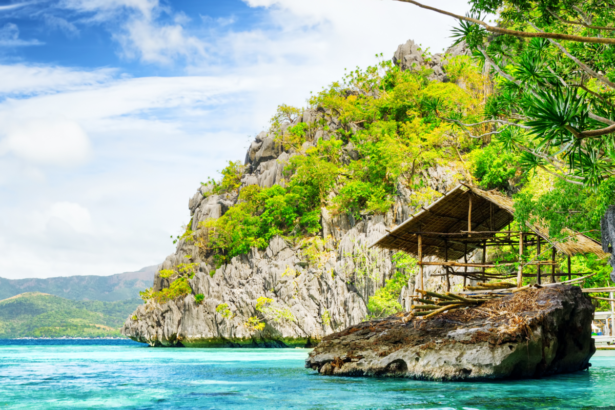 Paisagem de uma praia com enormes rochas e uma construção de casa com bambu 