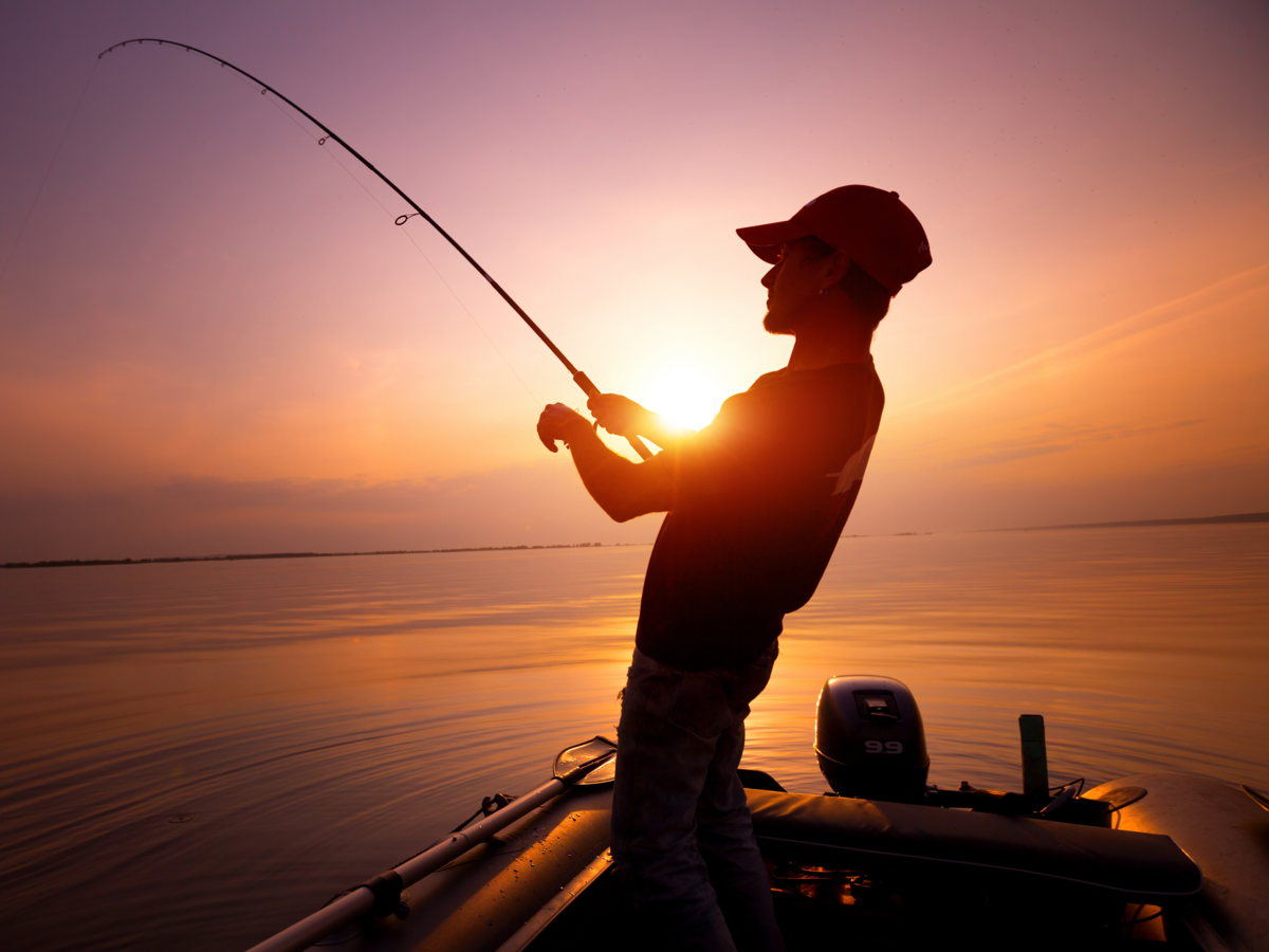 Pescador em cima de um barco no rio segurando vara de pescar