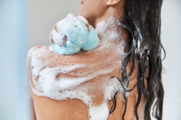 Mulher esfregando o ombro com uma esponja de banho