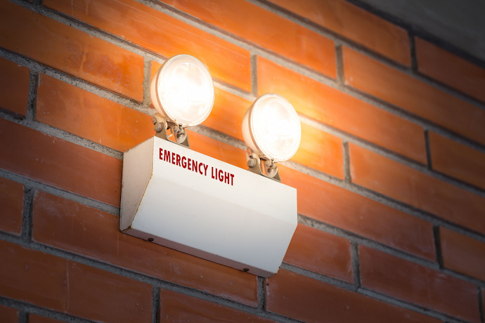 Gerador de luz ligado, emitindo as luzes e escrito "Emergency Light" colado a uma parede com formato de tijolos