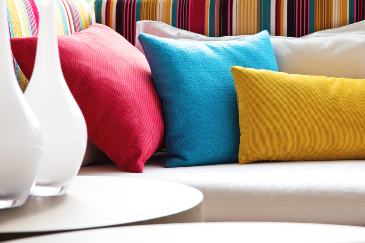 Três almofadas coloridas no sofá e ao lado dois vasos brancos