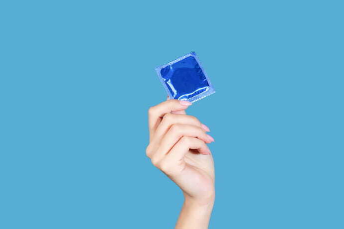 Mão segurando pacote azul de preservativo