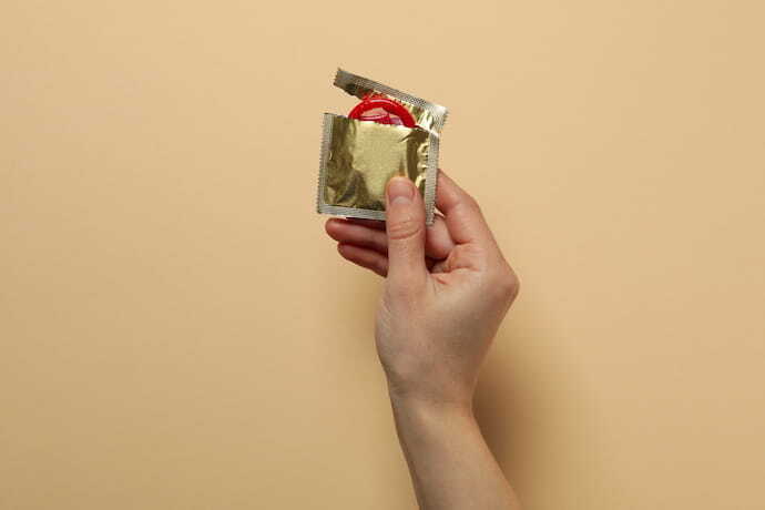 Mão segurando pacote aberto de preservativo