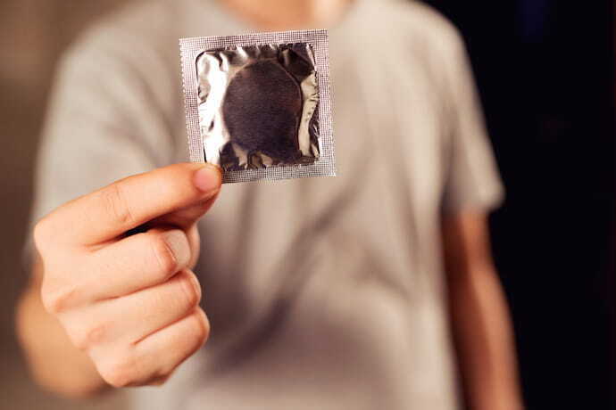 Homem segurando pacote cinza de preservativo