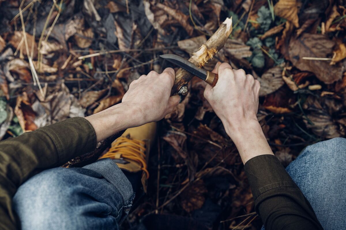 Praticante de bushcraft afiando pedaço de madeira com faca