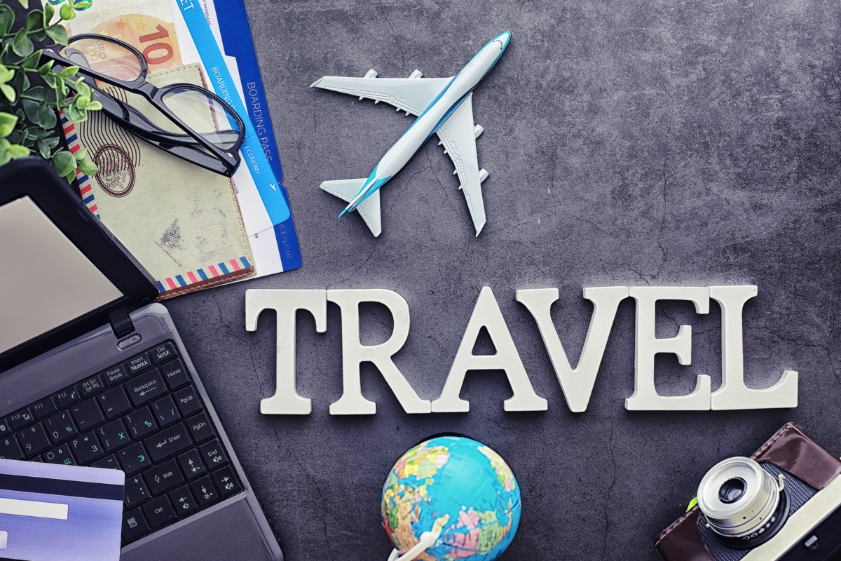 Sobre a mesa passaporte, óculos, avião, globo, câmera e notebook.