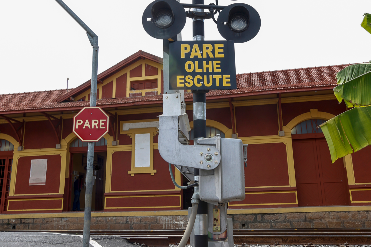 Fachada vermelha e amarela da Estação Ferroviário de Guararema com placa escrito "Pare, olhe, escute"