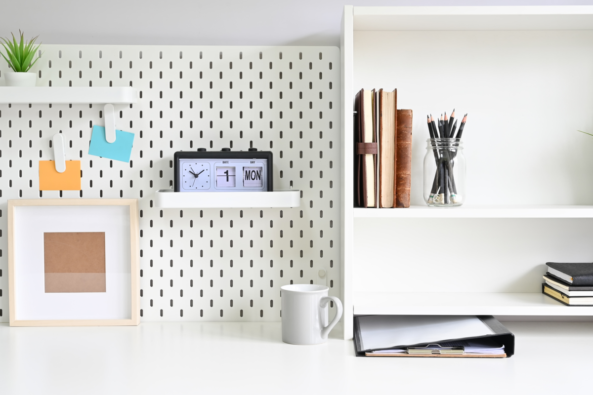 Prateleiras e pegboard com material de escritório na mesa.