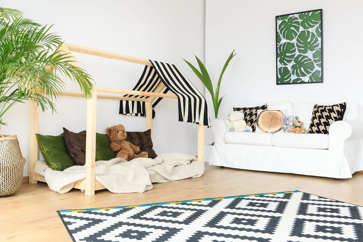 Quarto infantil com cama montessoriana e estrutura em formato de casinha, sofá branco, plantas e decorações verde, marrom e preto