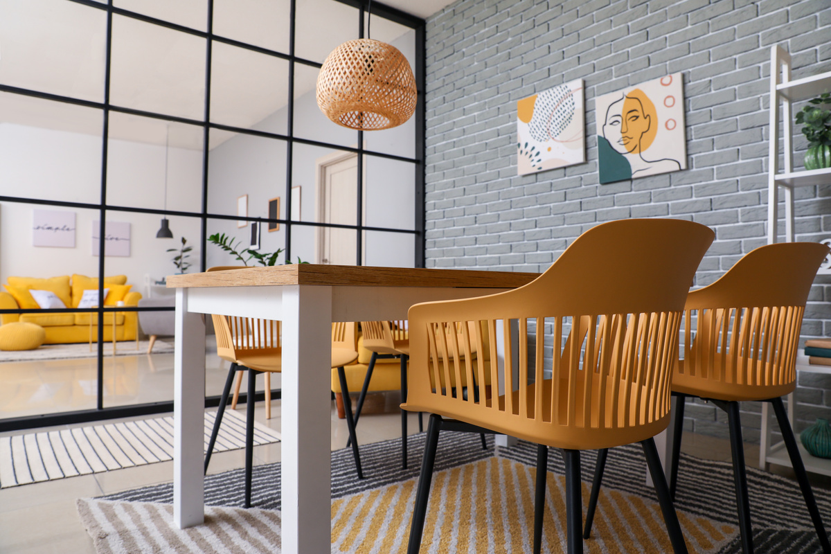 Uma sala de jantar com cadeiras marrons claras, mesa e um divisor de vidro