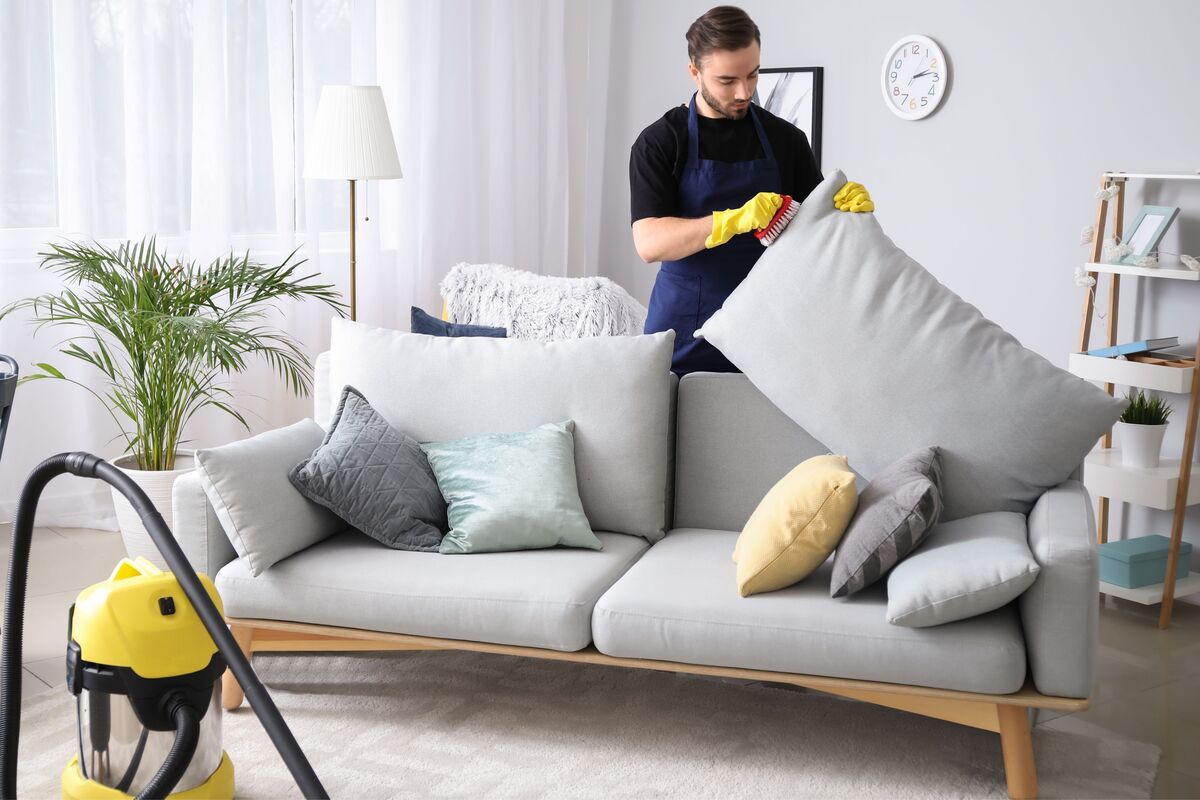 Homem limpando almofada do encosto de sofá