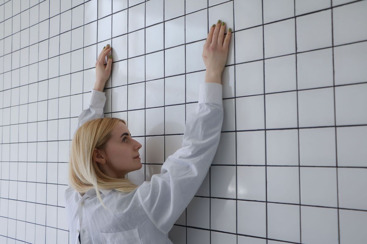 Mulher loira com os braços erguidos perto de uma parede de azulejos