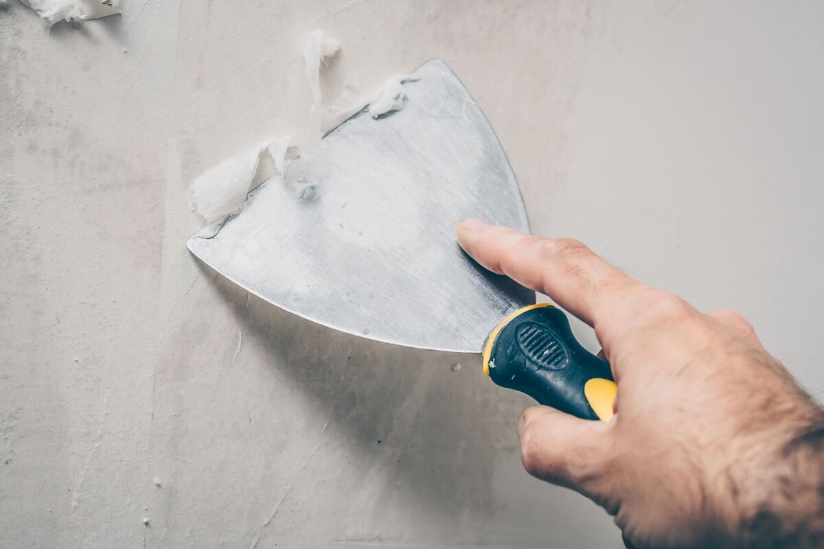 Pessoa removendo papel de parede antigo com espátula