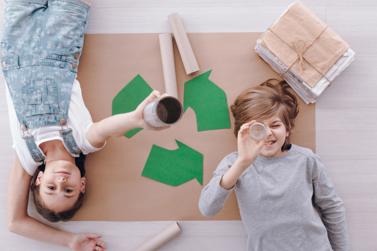 Duas crianças deitadas sobre o símbolo da reciclagem.