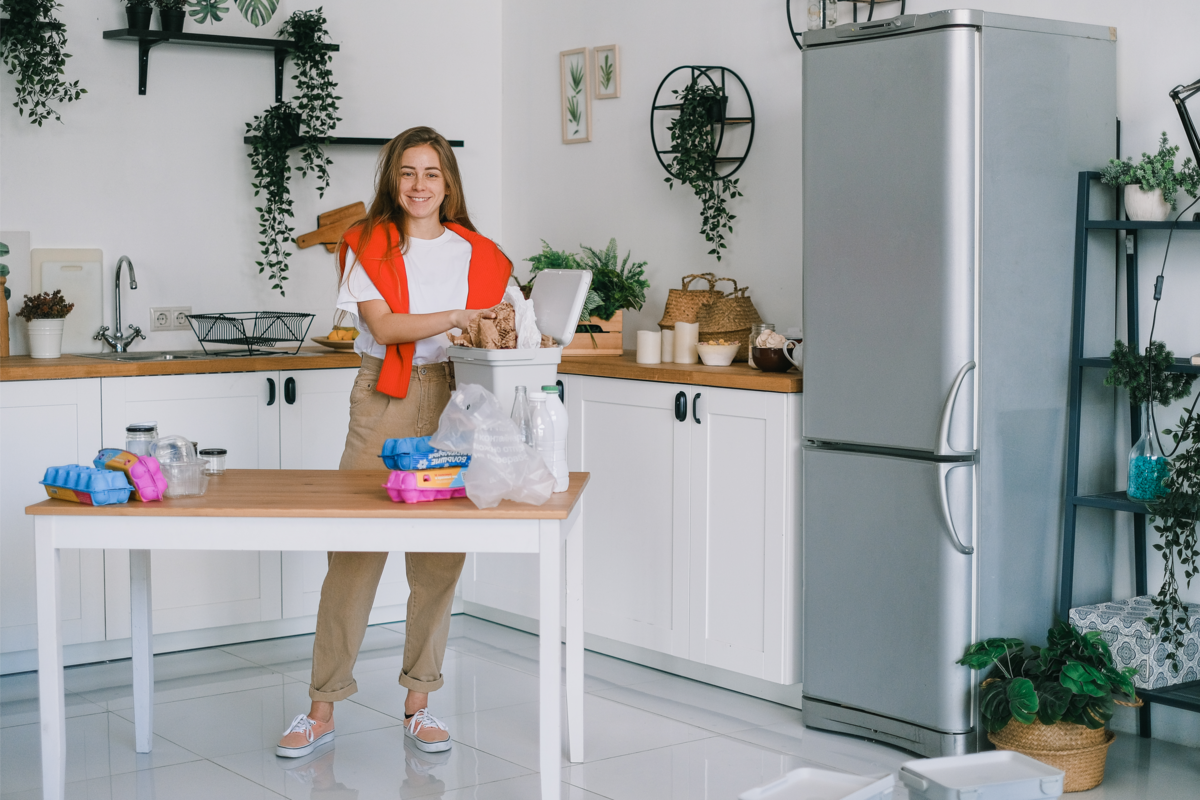 Mulher separando lixo, na cozinha branca decorada com plantas.