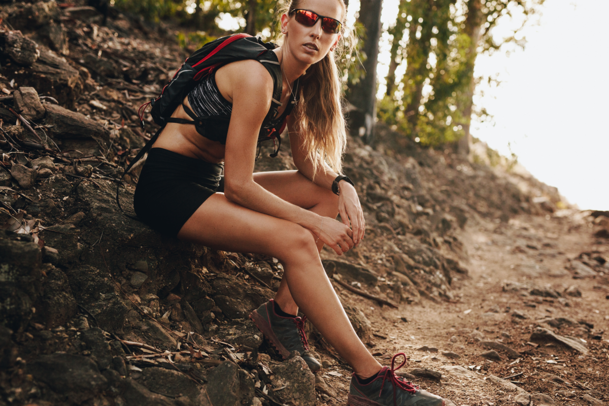 Uma mulher de óculos de sol sentada em uma rocha em uma trilha
