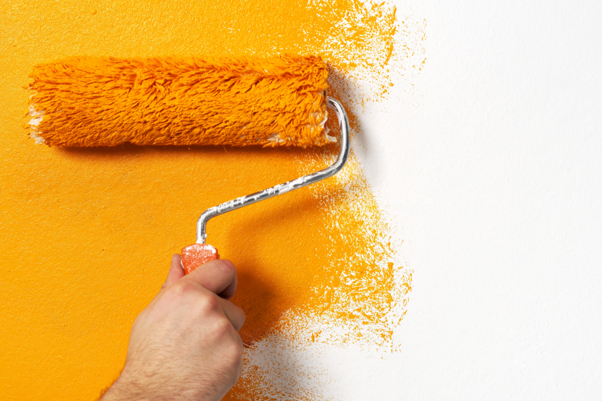 Indivíduo pintando a parede de amarelo com um rolo.