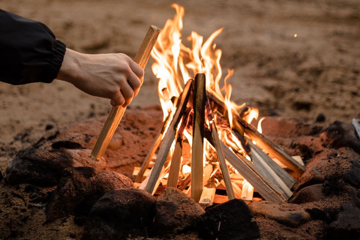 Pessoa adicionando gravetos em fogueira com formato de cone