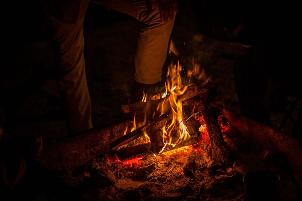 Pessoa em pé próxima à pequena fogueira com bastante chamas