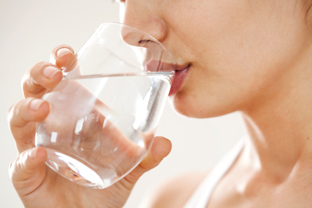 Mulher bebendo água em um copo de vidro.